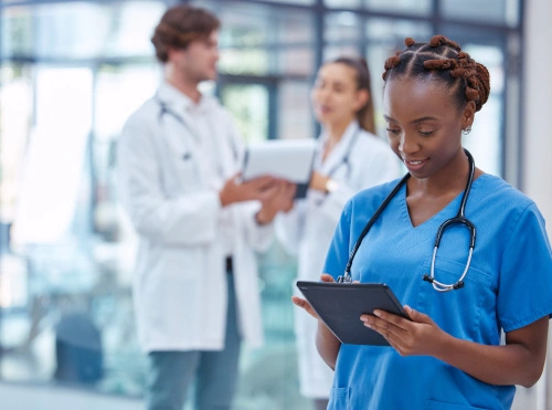 medical assistant in foreground using tablet with practitioners conversing in background